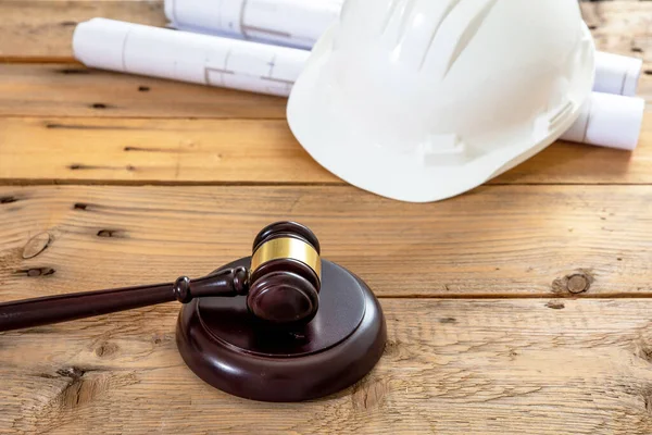 Construction, Labor law. White color engineer safety hardhat, judge gavel and building blueprint plans on wooden table