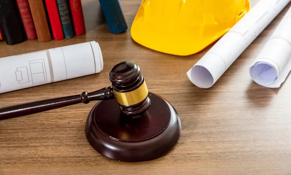 Construction and Labor law. Judge gavel and building drawings on wooden table, close up view.