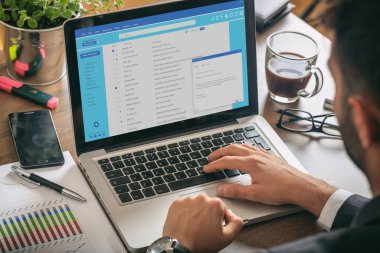 Email message communication. Man working with a computer, client mail list on laptop screen, office desk background.