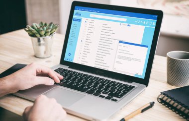 Email message communication. Man working with a computer, client mail list on laptop screen, office desk background.