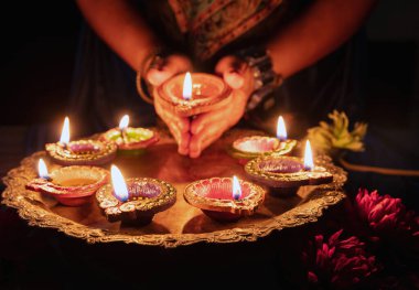 Diwali, Deepavali Hindu Festival of lights celebration. Diya oil lamp lit in woman hands, dark background. close up view.