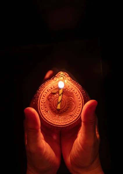 Diwali, Deepavali Hindu Festival of lights celebration. Diya oil lamp lit in woman hands, dark background. top view.