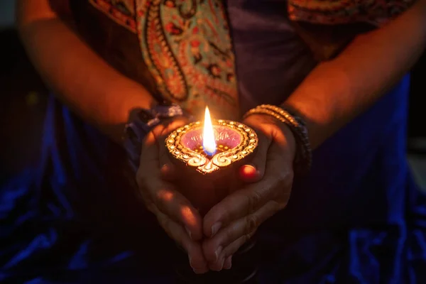 Diwali, Deepavali Hindu Festival of lights celebration. Diya oil lamp lit in woman hands, dark background. close up view.