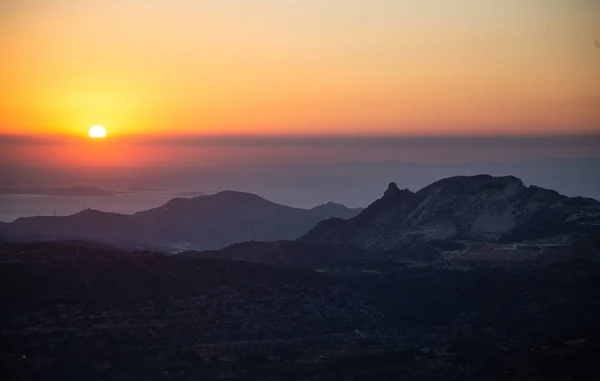 Sunset over Naxos island, Cyclades destination Greece. Nature quiets down concept. Sundown, behind hills silhouette, paints orange and gold yellow the sky background.