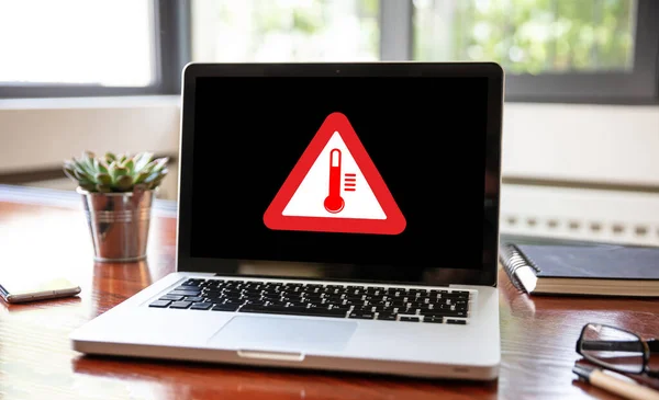 High temperature warning sign on a laptop screen.  Computer overheating concept. Heavy load and hot weather danger. Business office desk background.