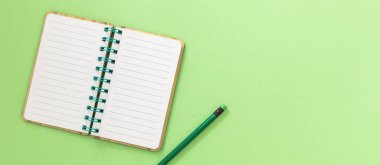 Boş, sarmal bir not defteri. Kağıt defter ve açık yeşil arka planda silgisi olan kalem. Metin için boşluk, genel görünüm