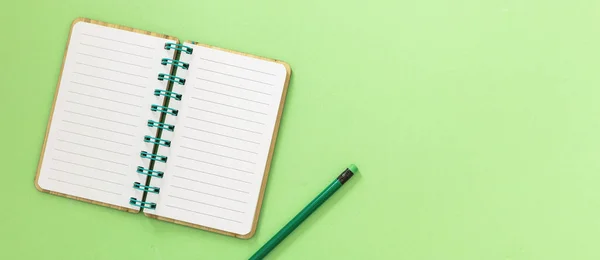 Blank open spiral notepad. Paper notebook and pencil with eraser on light green background. Space for text, overhead view