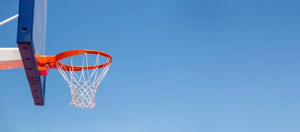 Basketball hoop, red ring and net on backboard, clear blue sky background, copy space. Sunny day, outdoors sport court