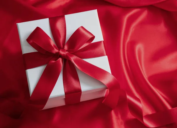 Valentine day giift, Christmas present. Overhead of white box with red ribbon and bow wrapping on satin background, curly decoration