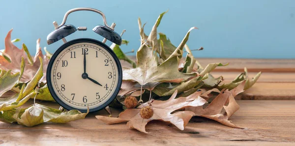 Fall Back Daylight Saving Time. Black alarm clock and autumn leaves on wooden table, copy spac