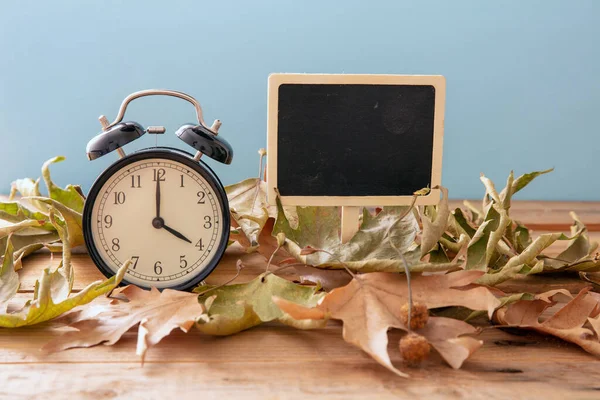 Fall Back Daylight Saving Time. Black alarm clock and autumn leaves on wooden table, copy spac