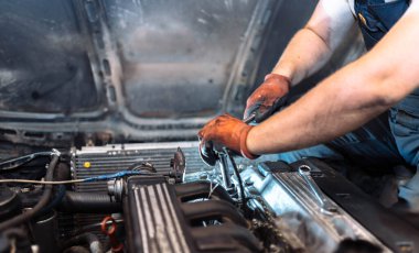 repairing a car engine in a car service, the hands of a mechanic unscrew the bolts