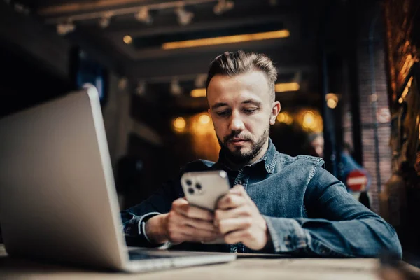 男性のフリーランサーは コワーキングカフェでスマートフォンで通信し モバイルアプリケーションをテストし オンライン作業 ストックフォト