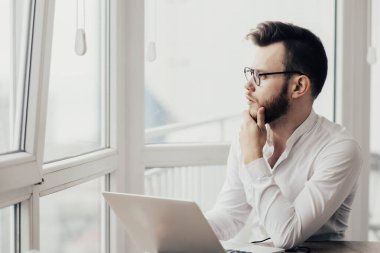 Beyaz gömlekli bir ofis çalışanı bilgisayarın başına oturur ve bir görev düşünür, entelektüel çalışma kavramı..