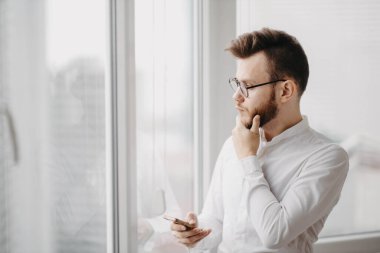 Gözlüklü ve sakallı bir adam ofisin penceresinde bir kriz olduğunu düşünüyor..