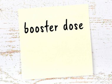 Yükseltici dozu hatırlatma kavramı. Tahta duvarda üzerinde yazı olan sarı yapışkan kağıt.