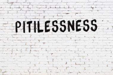 Beyaz tuğlalı duvar, siyah boyayla yazılmış acımasız yazı.