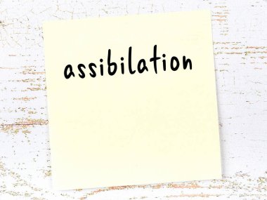 Tahta duvardaki sarı yapışkan notta el yazısıyla yazılmış asistanlık yazısı var.