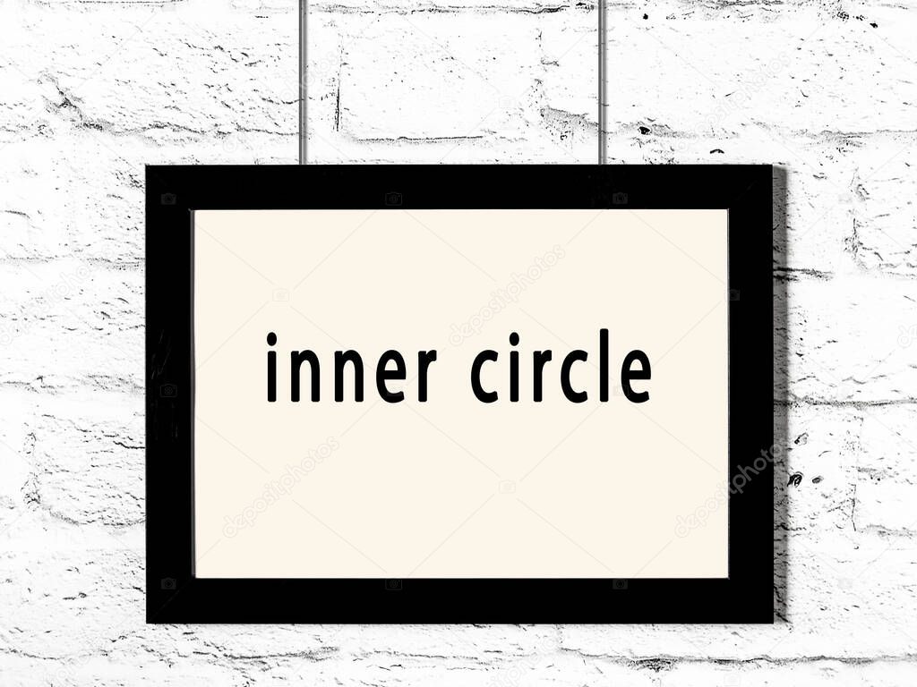 Black wooden frame with inscription inner circle hanging on white brick wall 