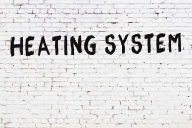 Siyah boyayla el yazısıyla yazması ısıtma sistemi olan beyaz tuğladan bir duvar.