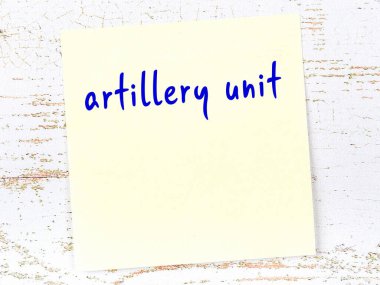 Tahta duvardaki sarı yapışkan notta el yazısıyla yazılmış topçu birliği var.