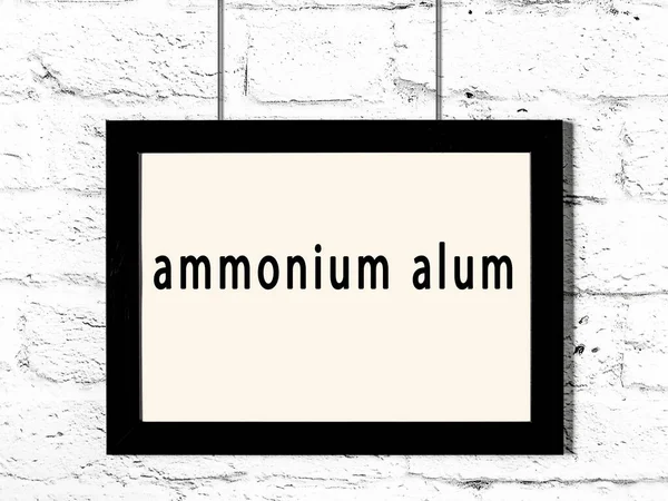Black Wooden Frame Inscription Ammonium Alum Hanging White Brick Wall — Stock Photo, Image