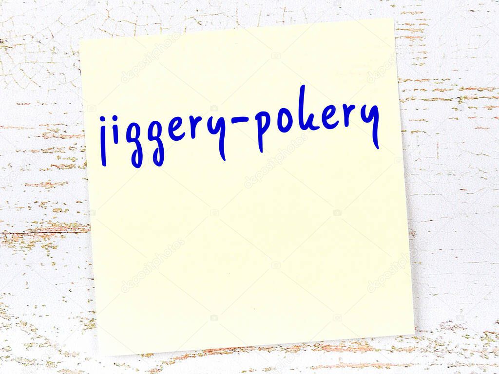 Yellow sticky note on wooden wall with handwritten inscription jiggery-pokery