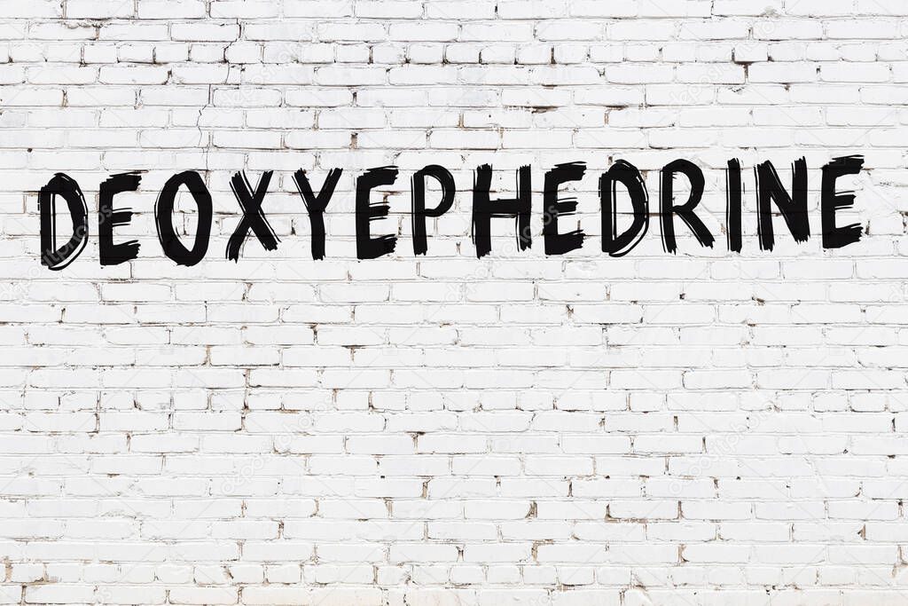 Inscription deoxyephedrine written with black paint on white brick wall.