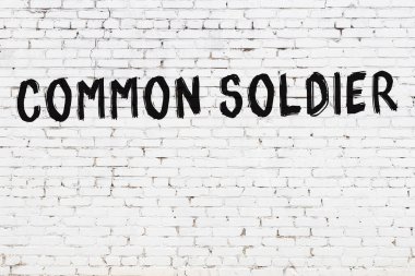 Yazılı beyaz tuğla duvar. Siyah boyalı sıradan asker el yazısı.