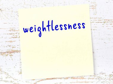 Ağırlıksızlıkla ilgili hatırlatma kavramı. Tahta duvarda üzerinde yazı olan sarı yapışkan kağıt.