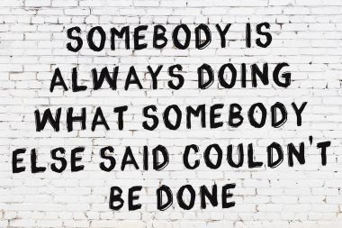 Beyaz tuğla duvara zekice alıntılar yazılı siyah bir yazı.