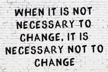 Beyaz tuğla duvara zekice alıntılar yazılı siyah bir yazı.