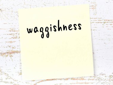 Concept of reminder about waggishness. Yellow sticky sheet of paper on wooden wall with inscription