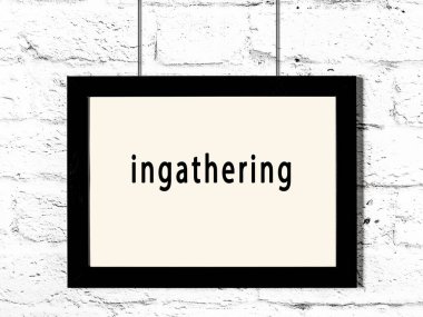 Black wooden frame with inscription ingathering hanging on white brick wall 