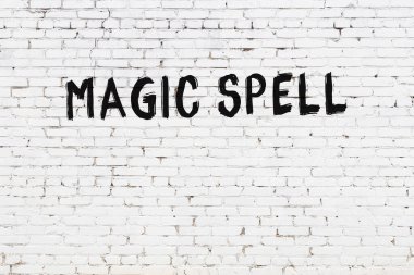 White brick wall with inscription magic spell handwritten with black paint