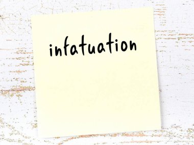 Yellow sticky note on wooden wall with handwritten inscription infatuation