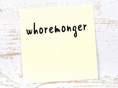 Concept of reminder about whoremonger. Yellow sticky sheet of paper on wooden wall with inscription