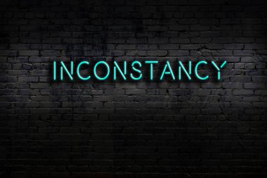 Neon sign with inscription inconstancy against brick wall. Night view