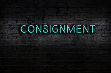 Neon sign with inscription consignment against brick wall. Night view