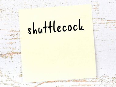 Yellow sticky note on wooden wall with handwritten inscription shuttlecock
