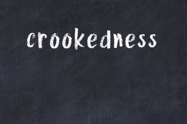 White brick wall with inscription crookedness handwritten with black paint