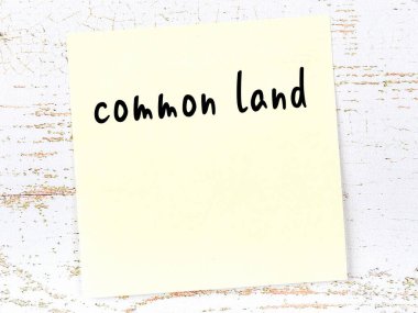 Concept of reminder about common land. Yellow sticky sheet of paper on wooden wall with inscription