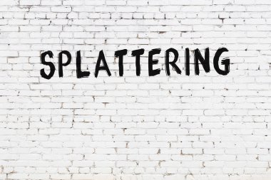 White brick wall with inscription splattering handwritten with black paint