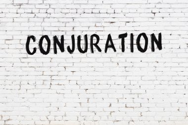 White brick wall with inscription conjuration handwritten with black paint