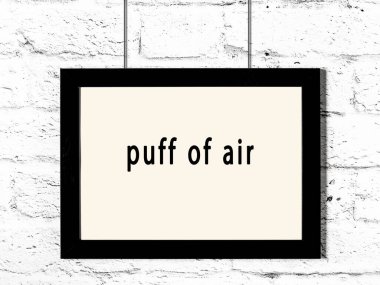 Black wooden frame with inscription puff of air hanging on white brick wall 