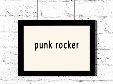 Black wooden frame with inscription punk rocker hanging on white brick wall 