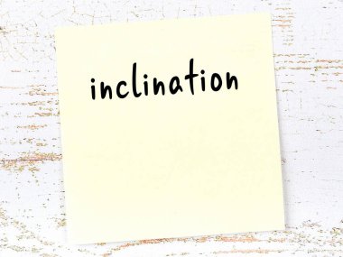 Concept of reminder about inclination. Yellow sticky sheet of paper on wooden wall with inscription