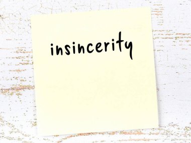 Concept of reminder about insincerity. Yellow sticky sheet of paper on wooden wall with inscription