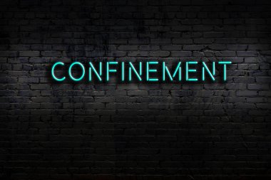 Neon sign with inscription confinement against brick wall. Night view