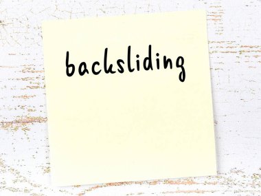 Yellow sticky note on wooden wall with handwritten inscription backsliding